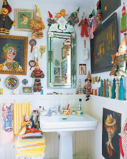 Eclectic bathroom decorated with clown art, puppets, and colorful vintage collectibles around a white pedestal sink