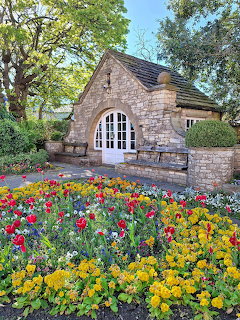 Stone cottage with white arched doors and colorful flower garden in foreground