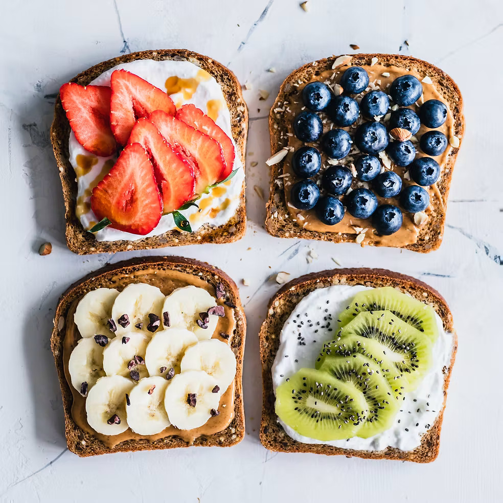 Four toast slices with strawberry, blueberry, banana, and kiwi toppings on marble surface