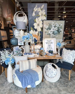 Blue and white home decor display with floral paintings, hydrangeas, pillows, vases, and textiles in a store