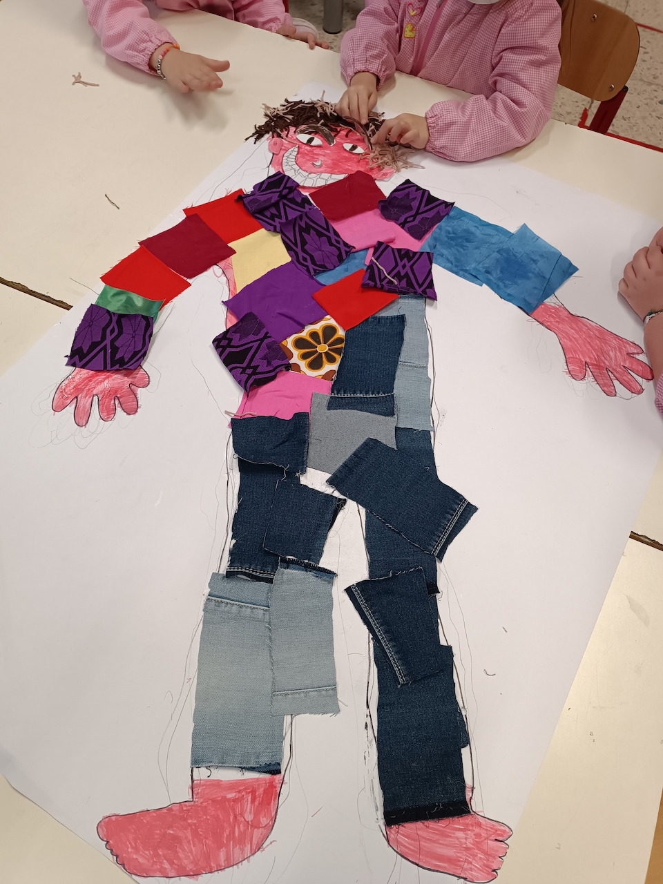 Children's collage of a human body figure assembled from colorful fabric and paper pieces on white paper