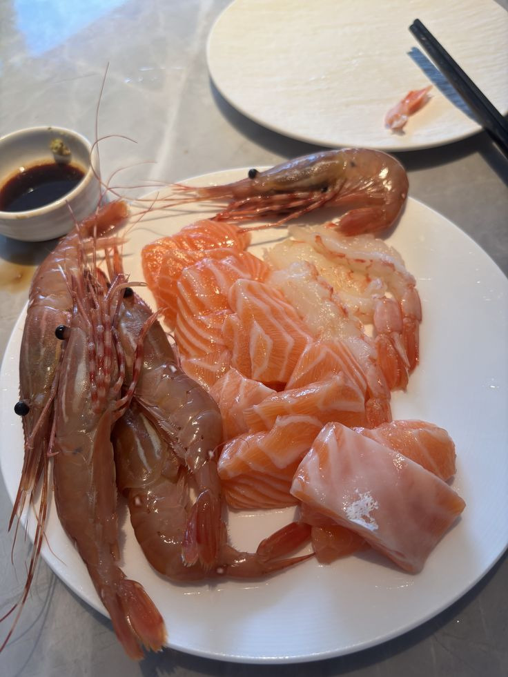Plate of salmon sashimi and raw shrimp with soy sauce and chopsticks