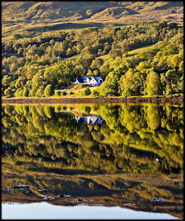 White house by Loch Eil with autumn trees and mirrored reflections in calm water