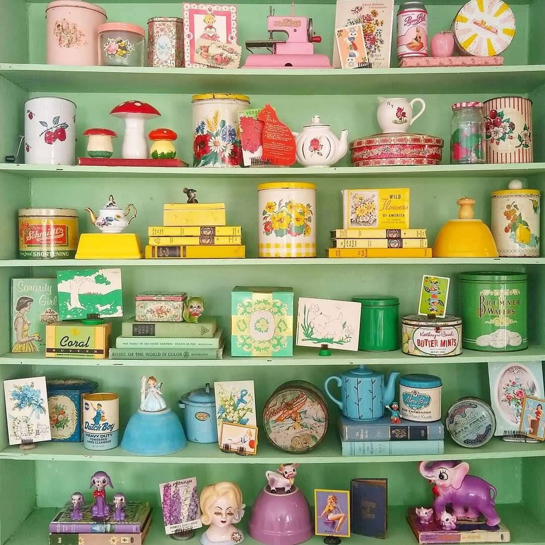 Mint green shelf with vintage colorful items arranged by rainbow hues including teapots, mugs, tins, books, and figurines