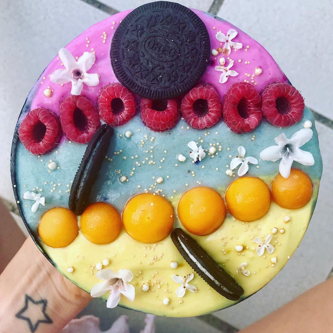 Overhead view of a colorful layered smoothie bowl with fruit and cookie toppings
