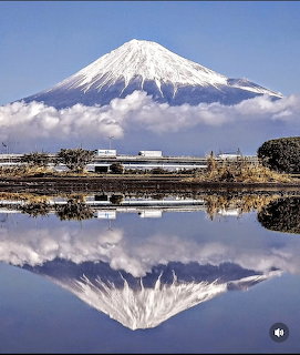 Snow-capped Mount Fuji reflected in calm water beneath a blue sky