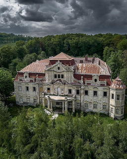 Abandoned ornate chateau with damaged roof surrounded by forest under dark storm clouds