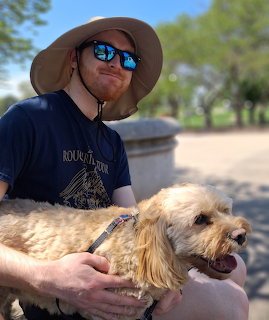 Man in hat and sunglasses holding a small fluffy dog outdoors
