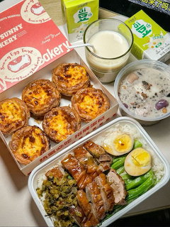 Korean meal spread with bento box, egg tarts, poridge, and soy milk on a table