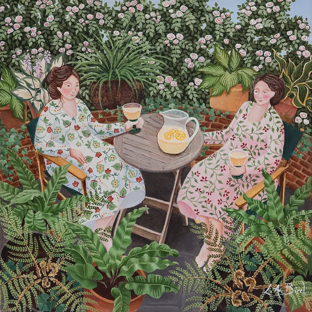 Two women in floral dresses having tea at garden table surrounded by plants and flowers