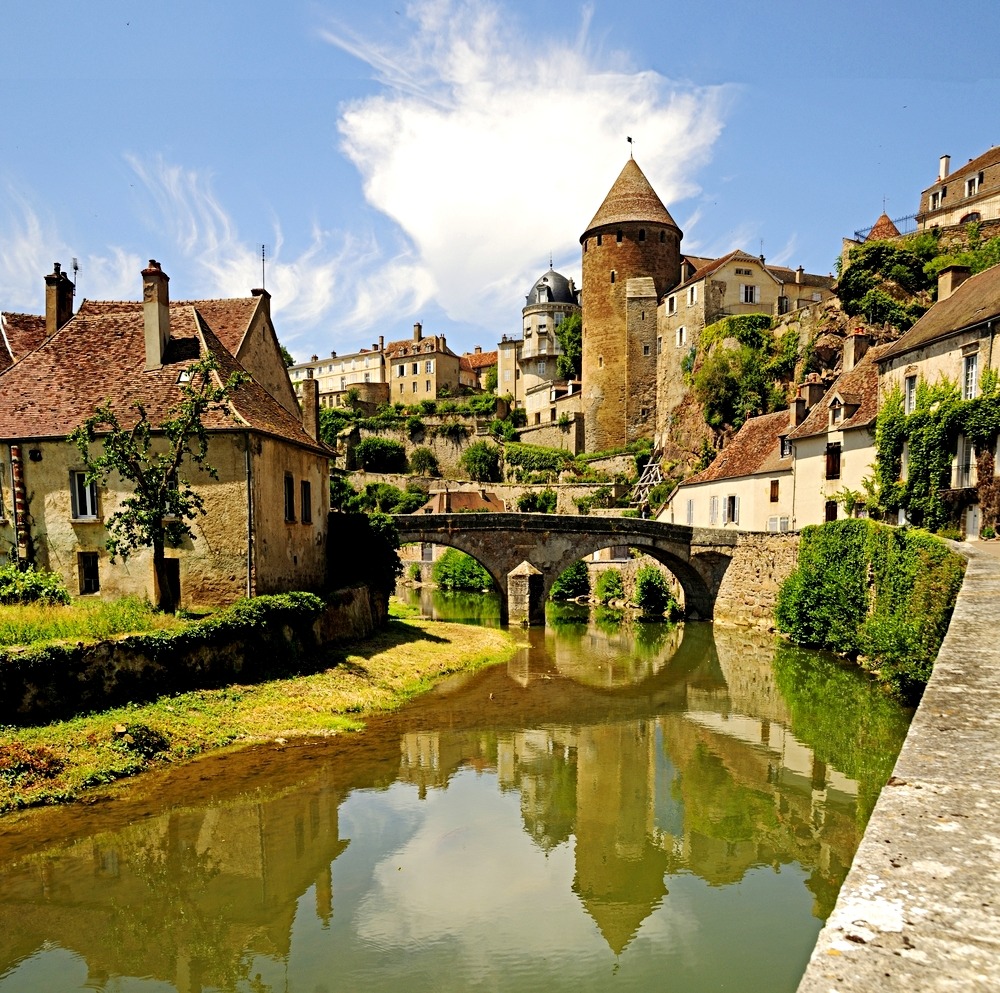 Medieval French village Semur-en-Auxois with stone bridge, tower, and houses reflected in river