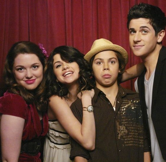 Four young people posing together in front of a red curtain