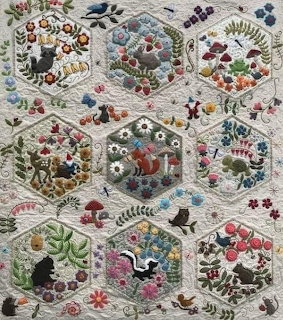 Embroidered quilt with hexagonal patches showing forest animals, birds, flowers, and plants in colorful hand-stitched folk art style