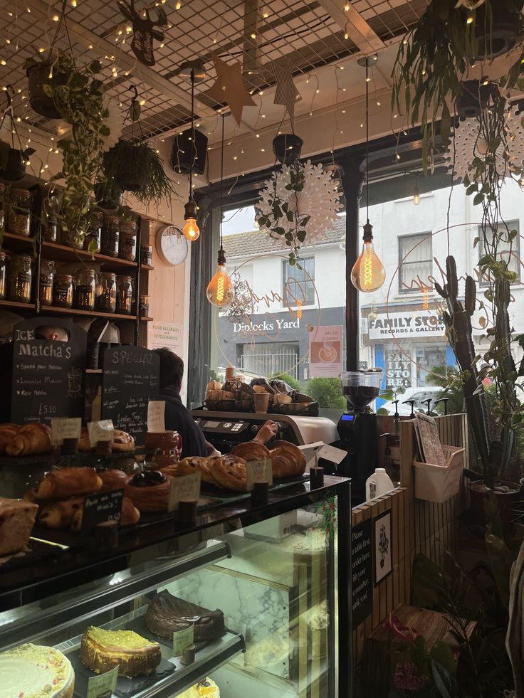 Cozy cafe interior with Edison bulb lighting, string lights, baked goods on display, and green plants