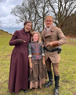 Three people in period clothing standing together outdoors in a Scottish highland setting