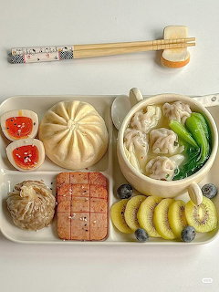 Tray of Korean-style food with dumplings, steamed buns, noodle soup, kiwi, and side dishes