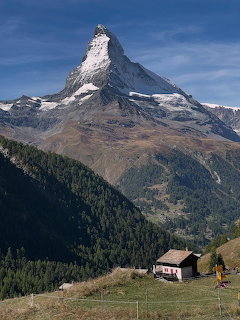 Matterhorn mountain peak with snow cap above green alpine meadow and wooden chalet in Zermatt Switzerland