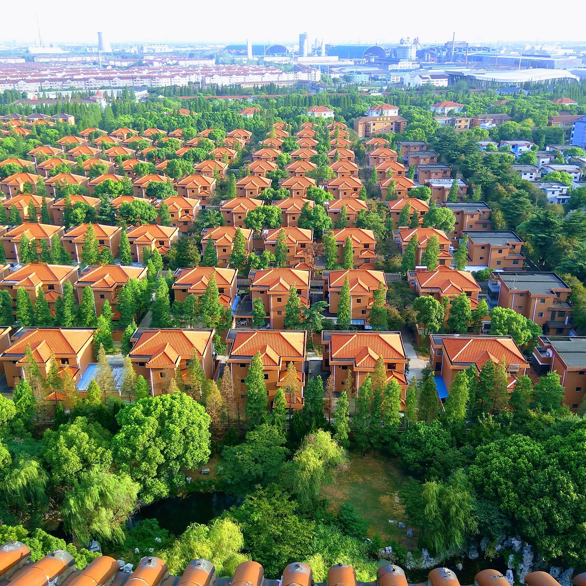 Aerial view of uniform red-roofed houses in rows surrounded by trees with industrial area in background