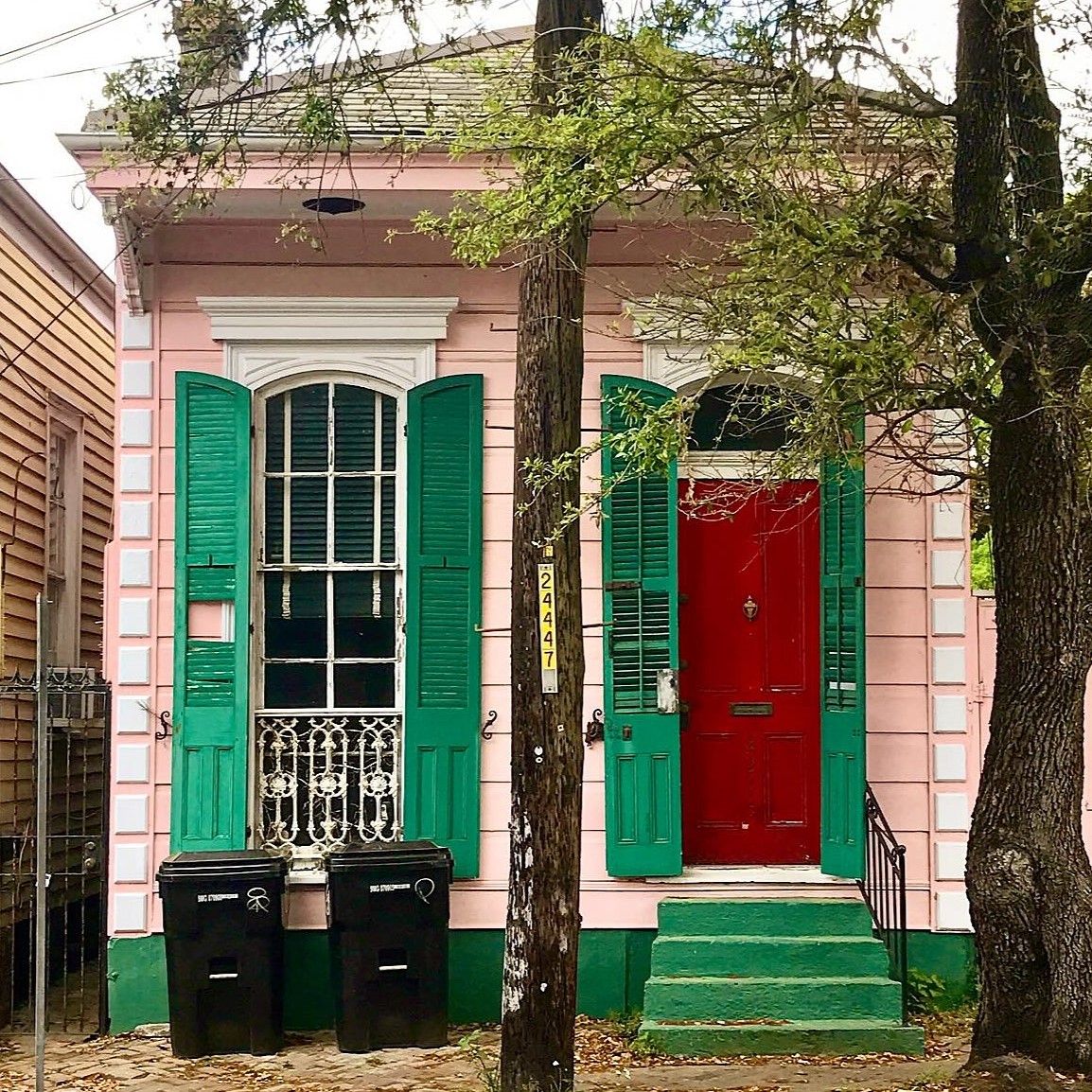 Small pink house with green shutters, red door, and green steps flanked by trees
