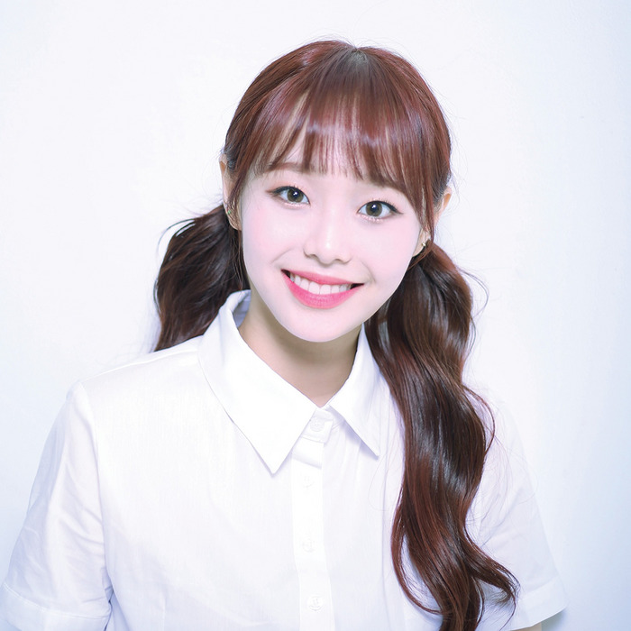Smiling young woman with brown pigtails in a white collared shirt against a light background