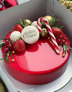 Glossy red Christmas cake decorated with berries, rosemary, a candy cane, and gold ornaments
