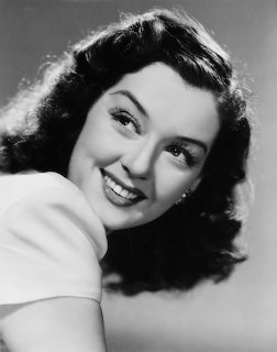 Black and white portrait of Rosalind Russell smiling with dark curled hair and white top