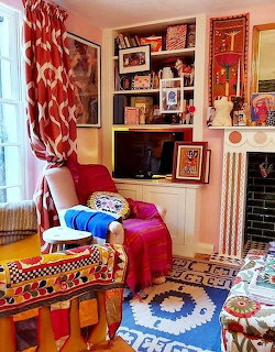Colorful eclectic living room with red armchair, patterned textiles, bookshelves, and framed art