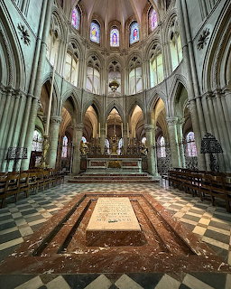 Gothic cathedral interior with ornate tomb monument, vaulted ceilings, columns, and stained glass windows