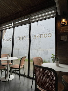 Cafe interior with wicker chairs, white tables, and large windows showing reversed Coffee Chill text