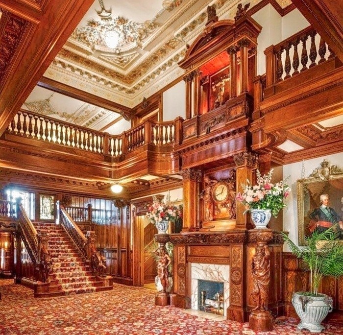 Grand historic interior with carved wooden staircase, ornate fireplace, and decorative ceiling