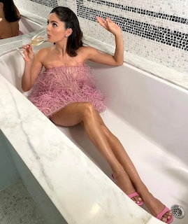 Woman in pink beaded dress reclining in white bathtub