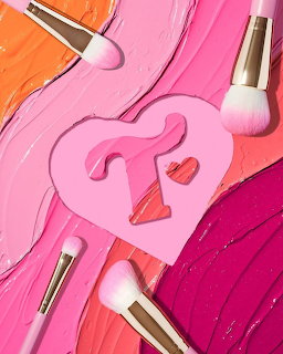 Pink makeup flat lay with cosmetic brushes, lipstick marks, and a heart-shaped paper cutout