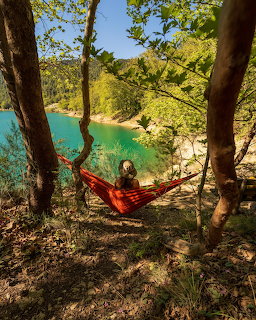 Person lying in red hammock between trees above turquoise lake with green forested shores