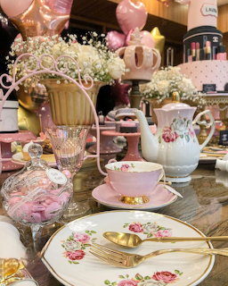 Pink floral tea set with teapot, teacup, plates and gold spoons on a decorated table