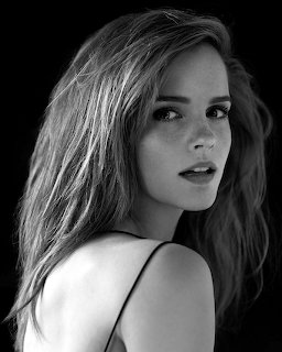 Black and white portrait of a woman with long hair looking over her shoulder against a dark background