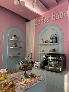 Pink and blue pastel cafe interior with arched shelves, espresso machine, and pastry display