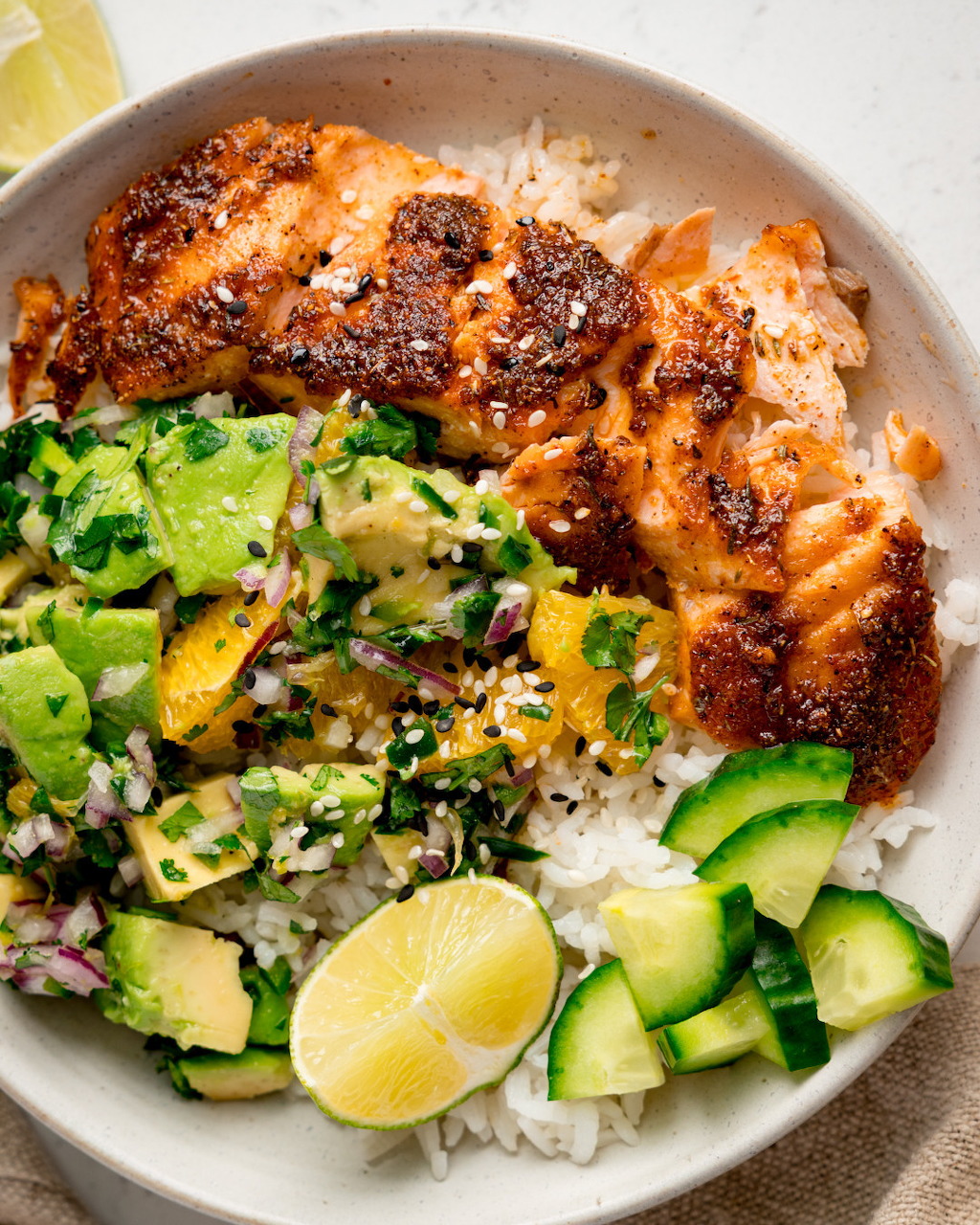 Bowl with seared salmon, white rice, avocado salsa, cucumber, and lime wedges