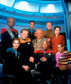 Star Trek Deep Space Nine cast in uniform on blue curved station set