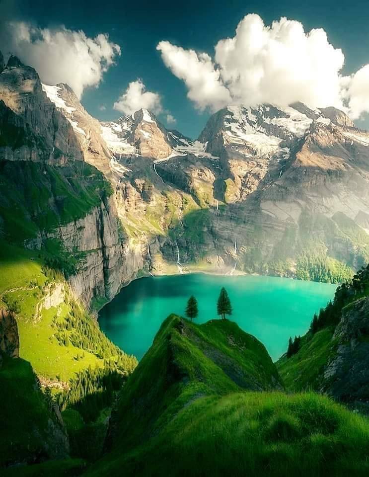 Turquoise alpine lake below green hills and snow-capped mountains