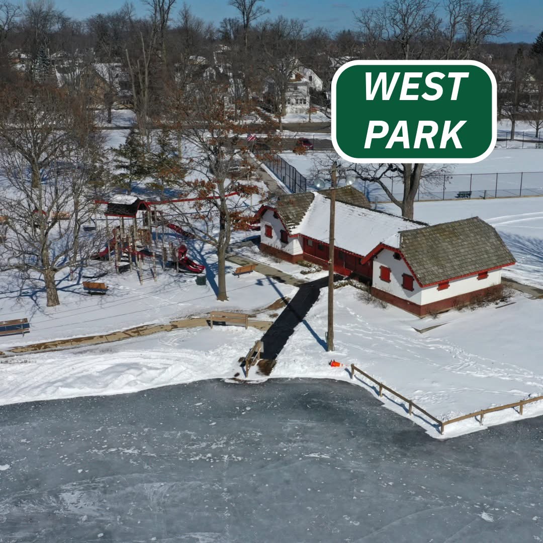 Aerial view of snowy West Park with frozen pond, red building, and bare winter trees
