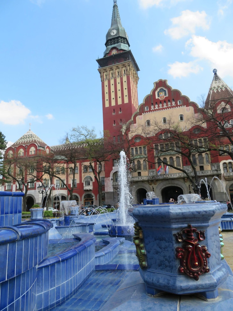 Ornate city hall building with tall tower and decorative blue fountain in town square
