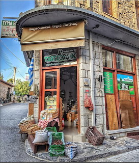 Corner shop with wooden doors and goods displayed on cobblestone street in traditional Greek stone building
