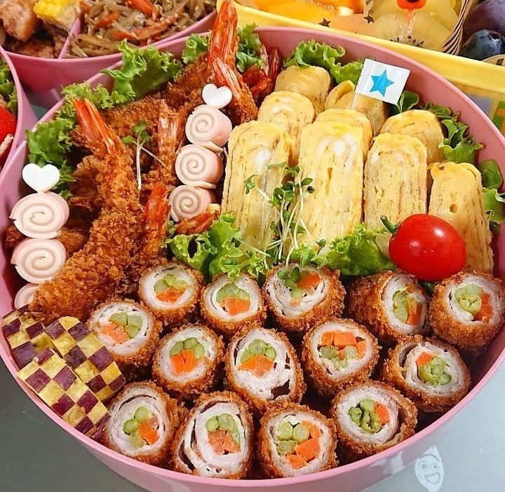Colorful bento box with sushi rolls, fried shrimp, egg slices, lettuce, and cherry tomatoes
