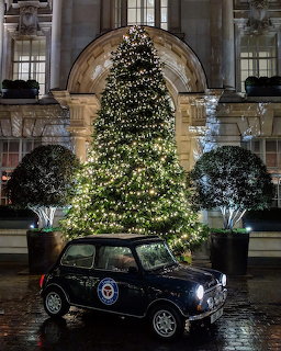 Dark blue classic Mini Cooper parked before a lit Christmas tree at a grand stone building entrance at night