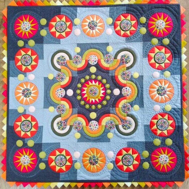 Colorful handmade quilt with symmetrical mandala pattern featuring flowers and curved geometric shapes