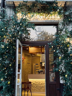 Café entrance decorated with leafy green plants and yellow fruits, glowing interior visible through glass door