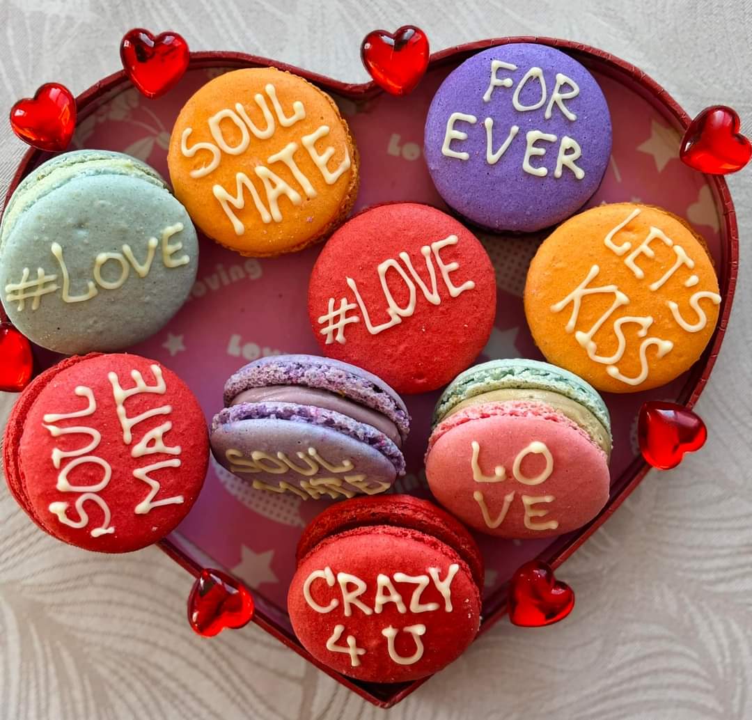 Heart-shaped arrangement of macarons with love messages and red heart decorations
