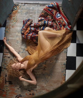 Overhead view of a woman in a golden dress lying on a floor with long red hair fanned out