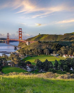 Golden Gate Bridge at sunset seen from green hills of Marin Headlands with bay and clouds