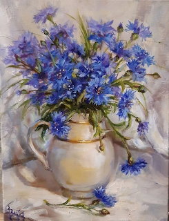 Oil painting showing blue cornflowers in a cream vase on draped fabric